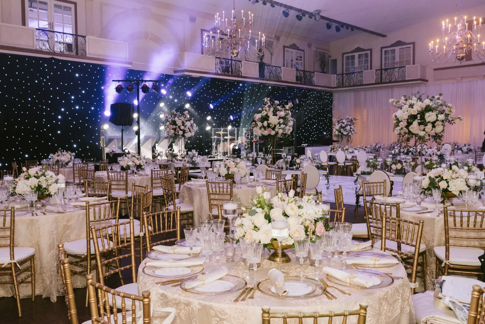 Large banquet hall with chandeliers, gold chairs and white floral centrepieces