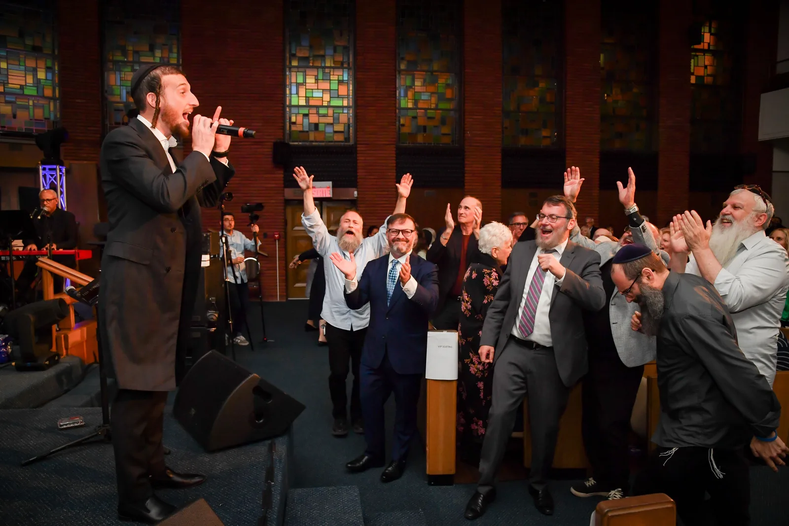A singer on the stage steps leads the crowd as men dance with raised hands below the sanctuary’s stained-glass windows