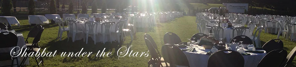 Tables set on the grass in Hampstead Park at dusk: the shul’s Shabbat Under the Stars banner